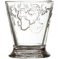 Clear glass tumbler featuring ornate embossed scallop shell motifs and swirling decorative flourishes above a textured base