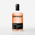 Product photography of an Empirical Symphony 6 spirit bottle filled with peach-hued liquid featuring a prominent black label detailing botanicals like Citrus Leaves and Fig Leaf against a clean white background
