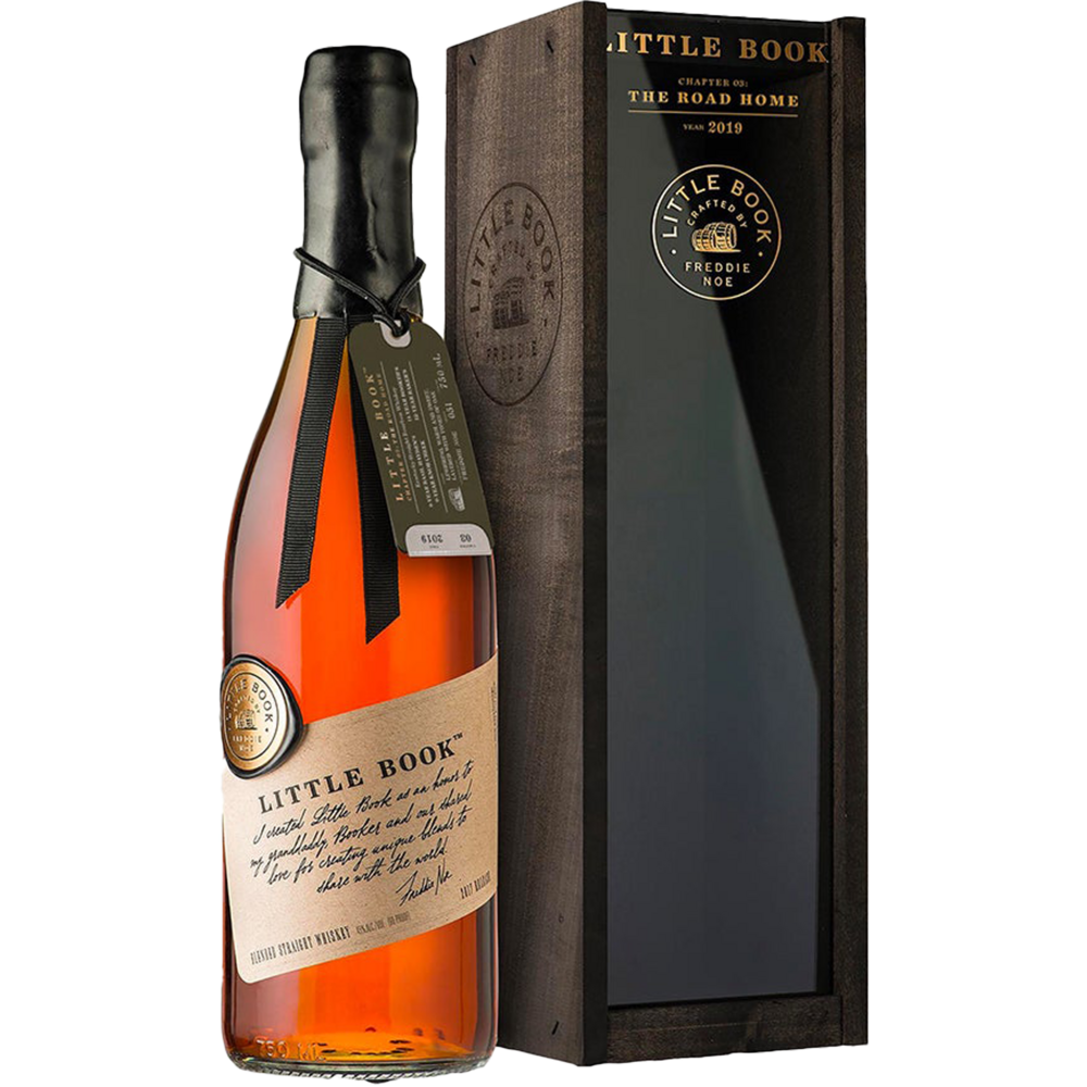 Product photograph of Little Book Chapter 03: The Road Home bourbon whiskey by Freddie Noe showing an amber liquid bottle with a craft paper label and black ribbon alongside a dark wooden display box with gold branding