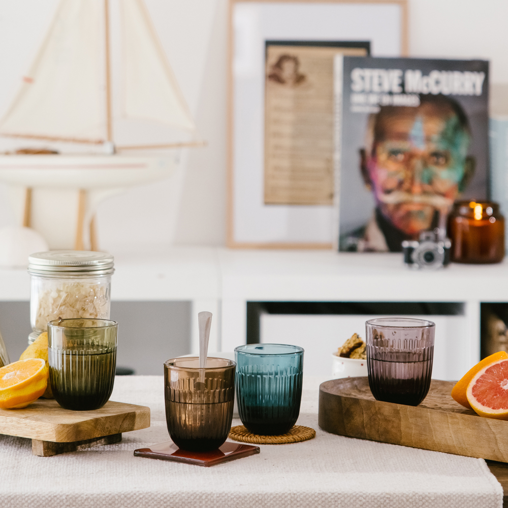 Photography of a vibrant home interior scene with amber, teal, and plum fluted glasses, fresh orange and grapefruit slices, and a Steve McCurry book cover on a white shelf