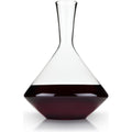 Clear glass wine decanter with a conical base and narrow neck filled with dark red wine on a white background with a subtle reflection