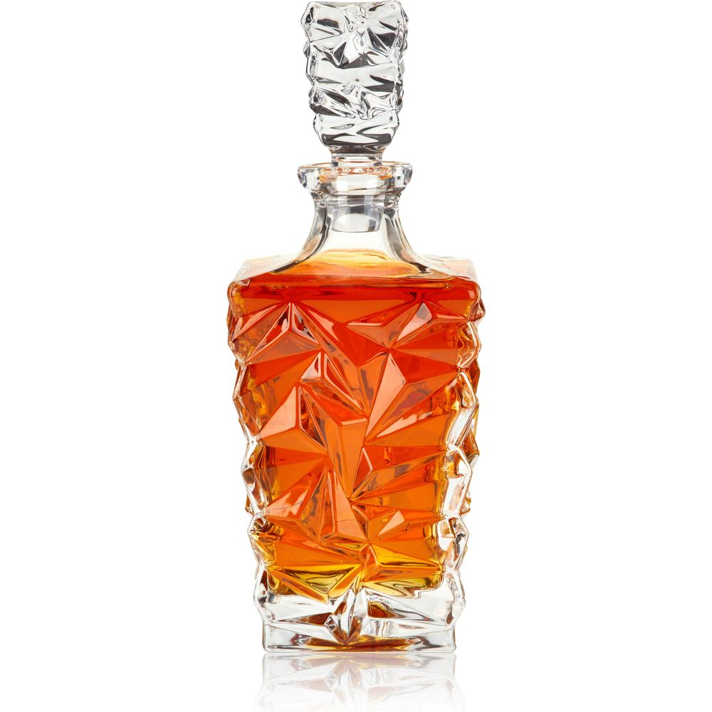 Digital photograph of a clear crystal whiskey decanter featuring an ornate geometric faceted design filled with glowing amber liquor and capped by a matching faceted stopper, presented on a reflective white surface