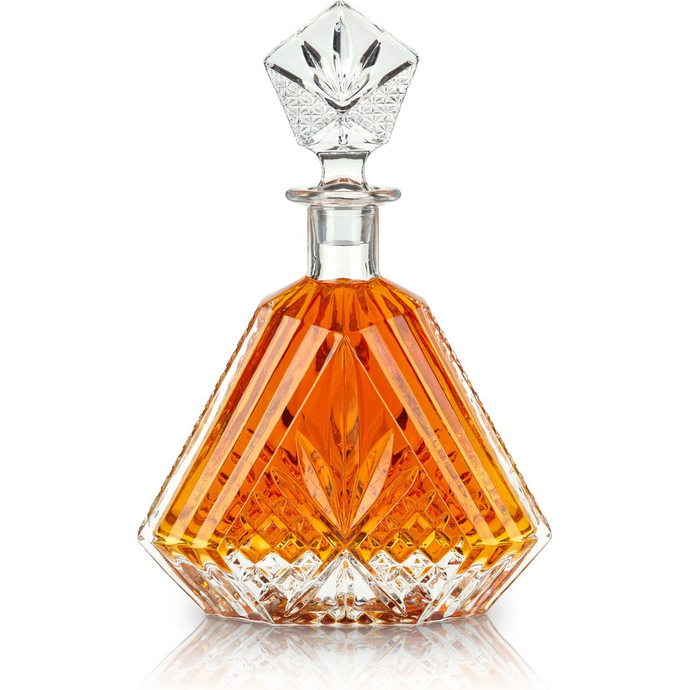 Clear crystal decanter with a diamond-shaped stopper and intricate geometric facets, filled with rich amber liquid, studio shot on a reflective white background