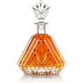 Clear crystal decanter with a diamond-shaped stopper and intricate geometric facets, filled with rich amber liquid, studio shot on a reflective white background