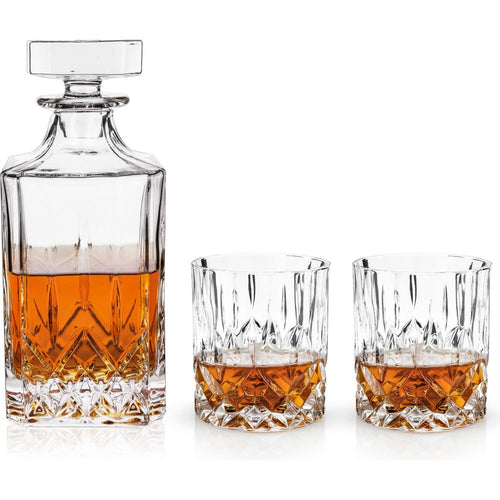 Cut crystal whiskey decanter and two matching tumblers on a white background, all containing amber liquid and featuring intricate geometric diamond-cut patterns