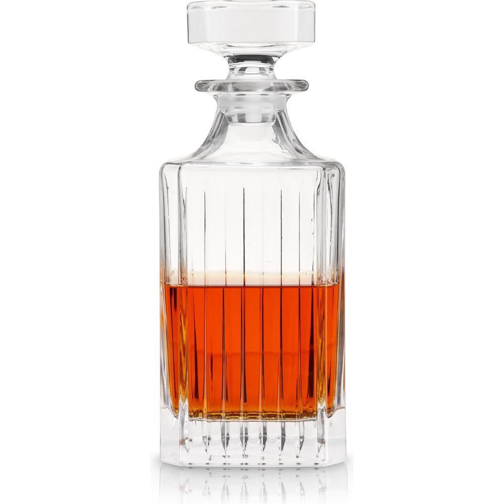 Clear crystal decanter with faceted stopper, vertical fluted design, and rich amber whiskey half-filling reflected on white background