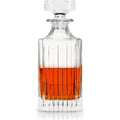 Clear crystal decanter with faceted stopper, vertical fluted design, and rich amber whiskey half-filling reflected on white background