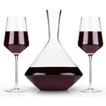 Clear glassware showcasing two elegant modern wine glasses and a unique geometric decanter, all filled with deep red wine against a clean white studio background