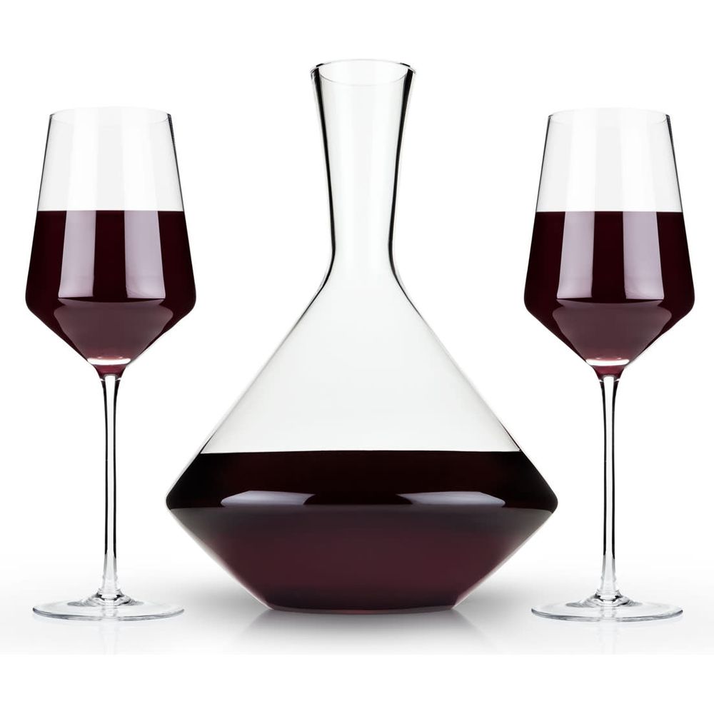 Clear glassware showcasing two elegant modern wine glasses and a unique geometric decanter, all filled with deep red wine against a clean white studio background