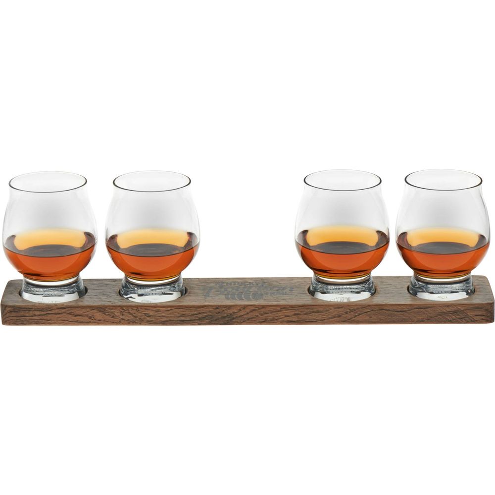 Photograph of four whiskey tasting glasses filled with amber whiskey on a dark wooden flight tray featuring an engraved Kentucky Bourbon Trail logo